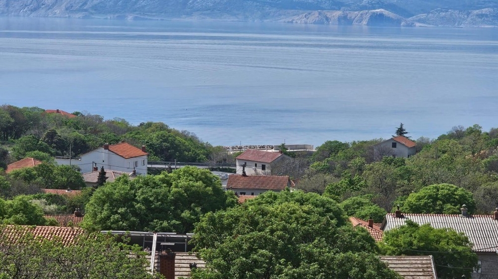 Blick auf die Dächer roter und weißer Häuser mit grünen Bäumen im Vordergrund und einem Blick auf das Meer im Hintergrund, ideal für Immobilien in Kroatien