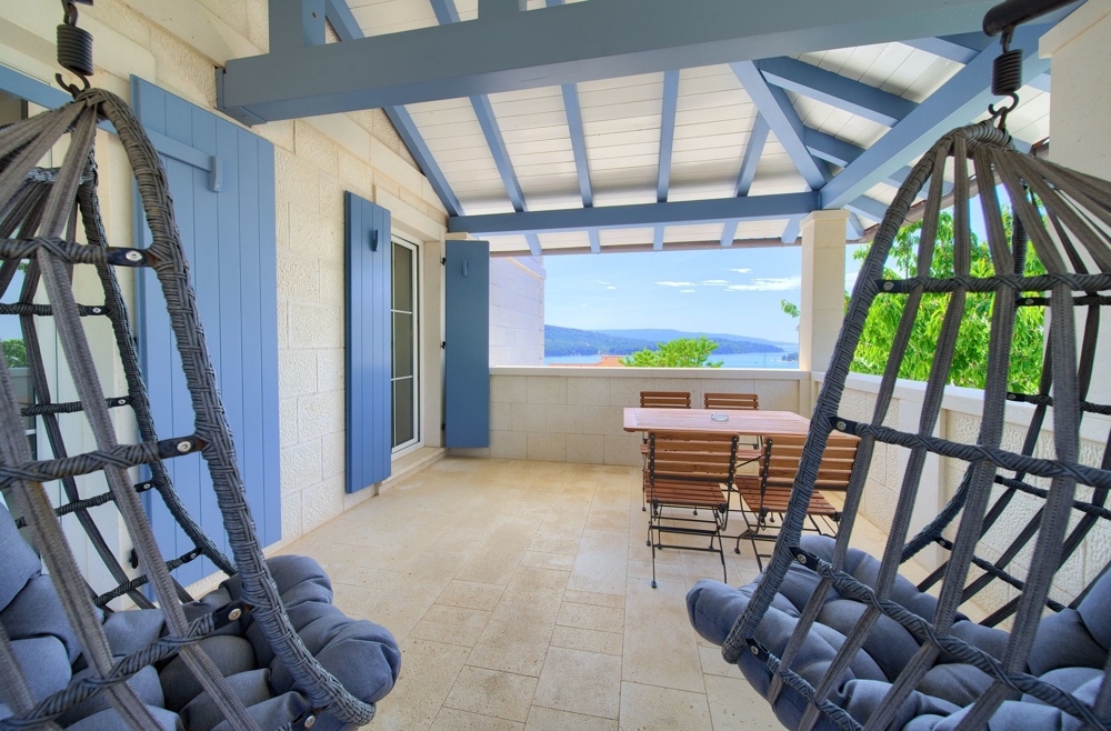 Terrasse mit Meerblick in einem Immobilienangebot in Kroatien, mit zwei hängenden Eierschaukeln und einem Esstisch unter einem offenen, schattigen Pavillon