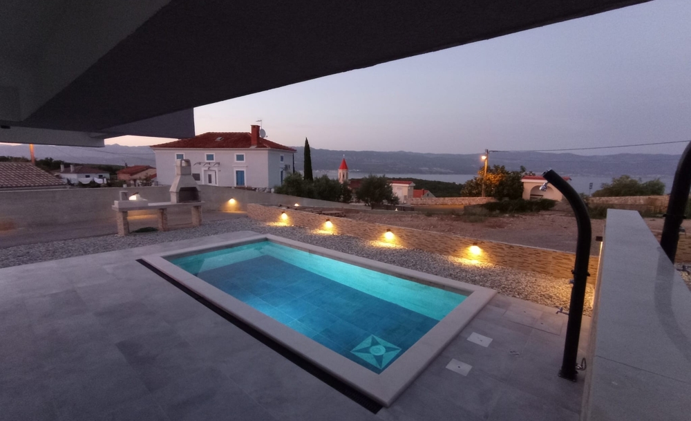 Abendansicht einer Immobilie in Kroatien mit beleuchtetem Pool und Blick auf das Meer im Hintergrund.