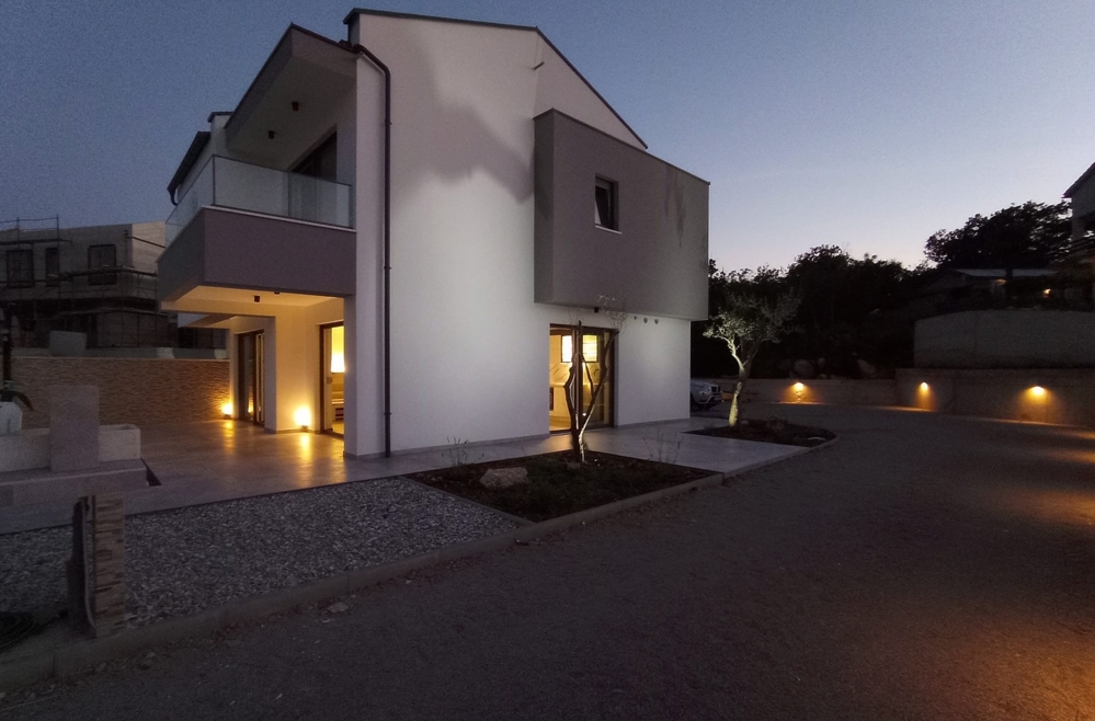 Seitenansicht einer Immobilie in Kroatien im Dämmerlicht mit beleuchtetem Pfad und Eingang.