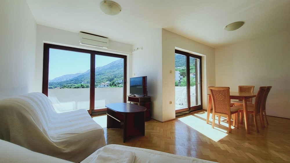 Wohnzimmer mit Sofa, Esstisch und Fenstertüren zum Balkon