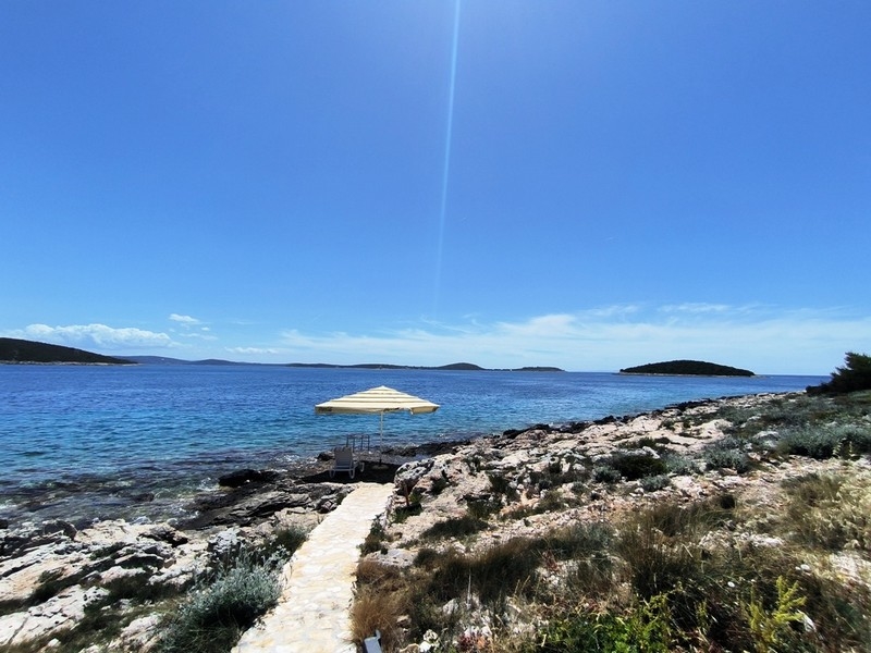 Immobilien Kroatien, Haus direkt am Meer - Panorama Scouting H3015: Weg führt zu einem felsigen Ufer mit einem Sonnenschirm und dem Meer im Hintergrund.