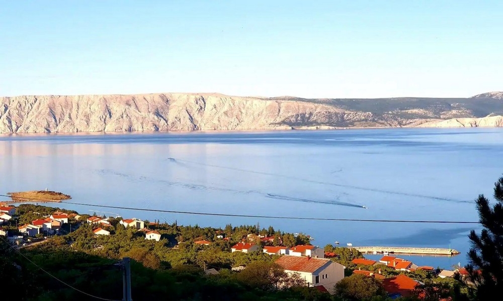 Panorama Scouting H3021 - Mehrparteienhaus mit Meerblick, zeigt eine wunderschöne Küstenlandschaft mit Häusern und einem ruhigen Meer vor einer Kulisse aus felsigen Hügeln.