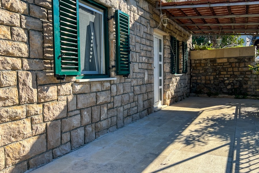 Steinterrasse mit Zugang zum Haus und grünen Fensterläden