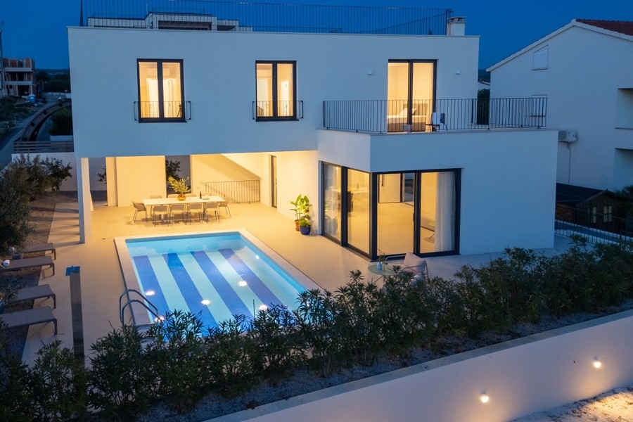 Moderne Villa mit beleuchtetem Pool und Terrasse bei Nacht