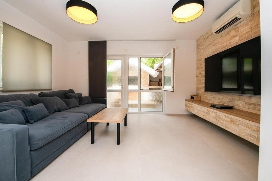 Modernes Wohnzimmer mit Sofa, TV-Wand und Zugang zur Terrasse