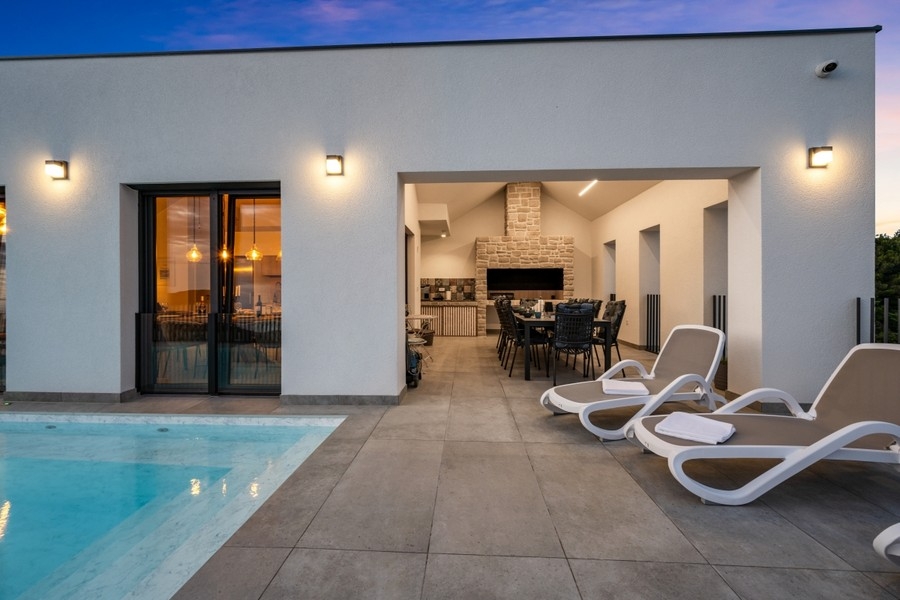 Überdachte Terrasse mit Sonnenliegen und Pool am Abend