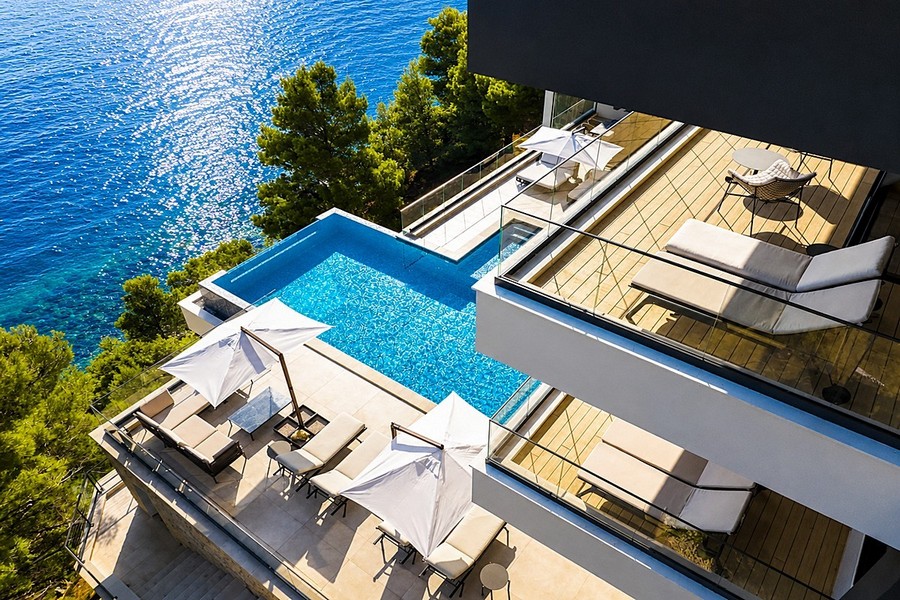 Blick von oben auf Pool und Terrassen am Meer
