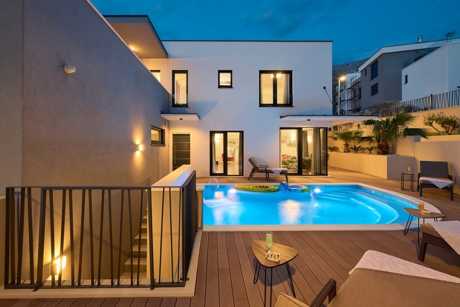 Poolbereich mit Holzdeck und beleuchteter Villa