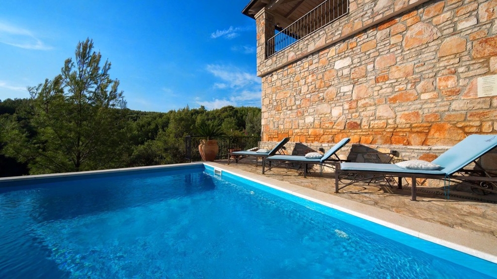 Swimmingpool mit Sonnenliegen an der Steinfassade