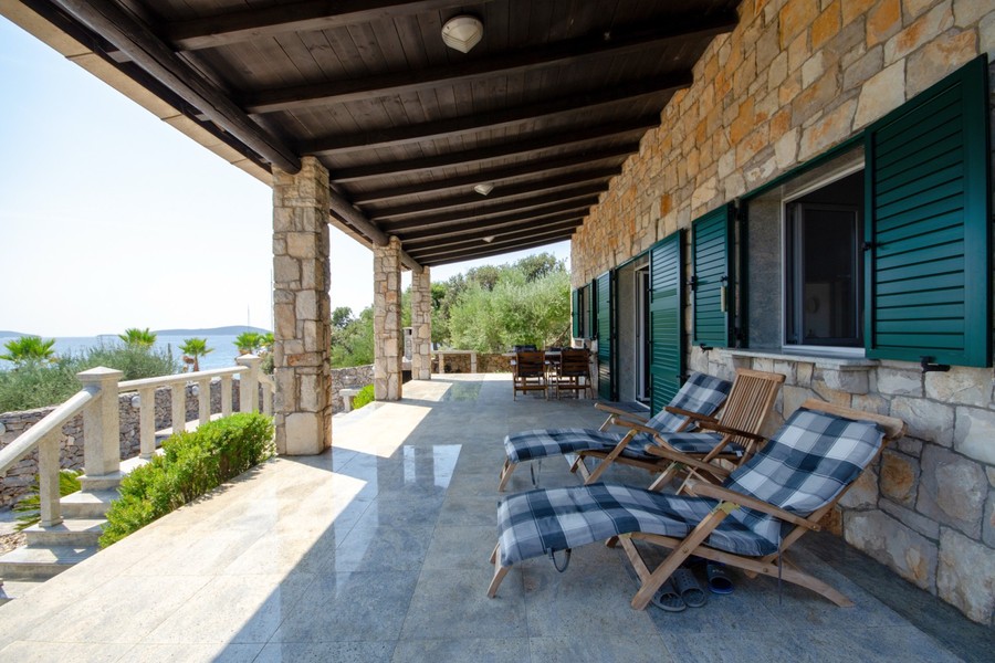 Überdachte Terrasse mit Liegestühlen an der Steinvilla