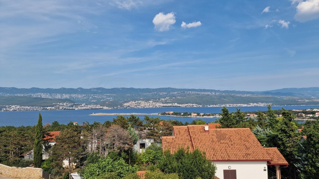 Blick über Dächer und Bäume auf Bucht und Gebirge