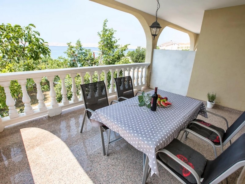 Überdachte Terrasse mit Meerblick, Tisch mit gepunkteter Tischdecke und sechs Stühlen, umgeben von üppigem Grün.