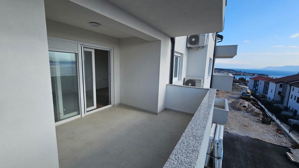 Balkonblick von einem zum Verkauf stehenden Apartment in Crikvenica, mit Blick auf umliegende Gebäude und das Meer.