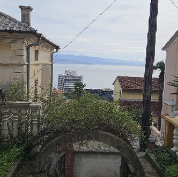 Blick auf das Meer durch eine Öffnung zwischen Gebäuden mit einem großen Schiff in der Ferne