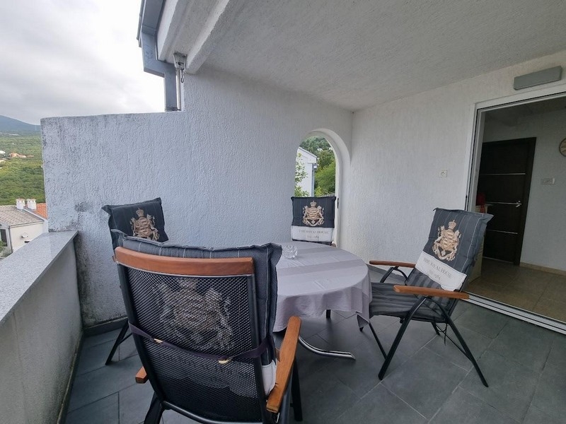 Überdachter Balkon mit Tisch und Stühlen und Bogenfenster, Blick auf grüne Bäume und teilweise Meerblick