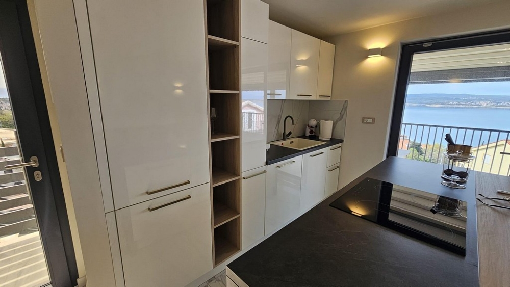 Moderne Küche in einem Appartement in Kroatien mit weißen Schränken, dunkler Arbeitsplatte und eingebauten Geräten. Immobilie Kroatien, Appartement mit Meerblick