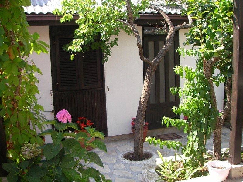 Ein idyllischer Innenhof mit blühenden Pflanzen und einem kleinen weißen Haus mit dunklen Fensterläden