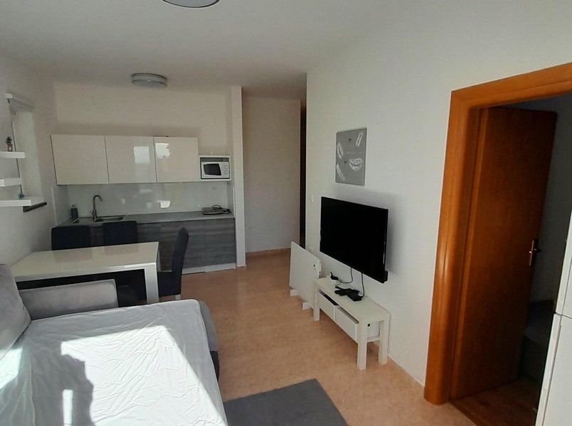 Wohnzimmer mit Fernseher, Esstisch und Zugang zum Schlafzimmer