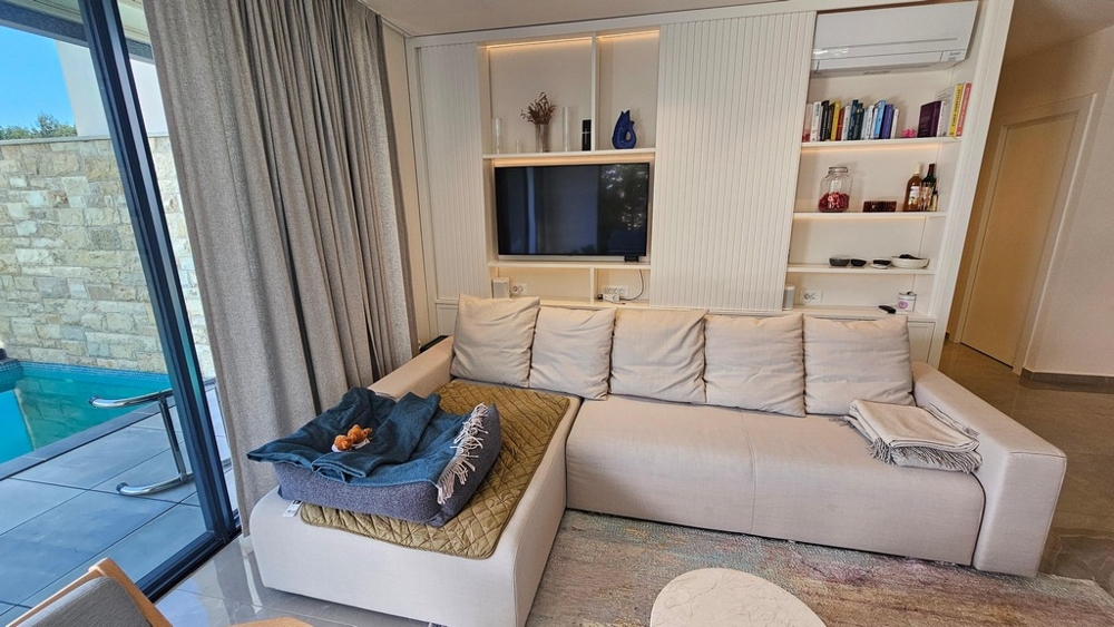 Wohnbereich mit Sofa, Fernseher und Poolzugang