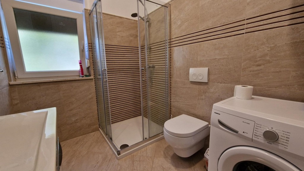 Badezimmer mit Duschkabine und Waschmaschine in Njivice
